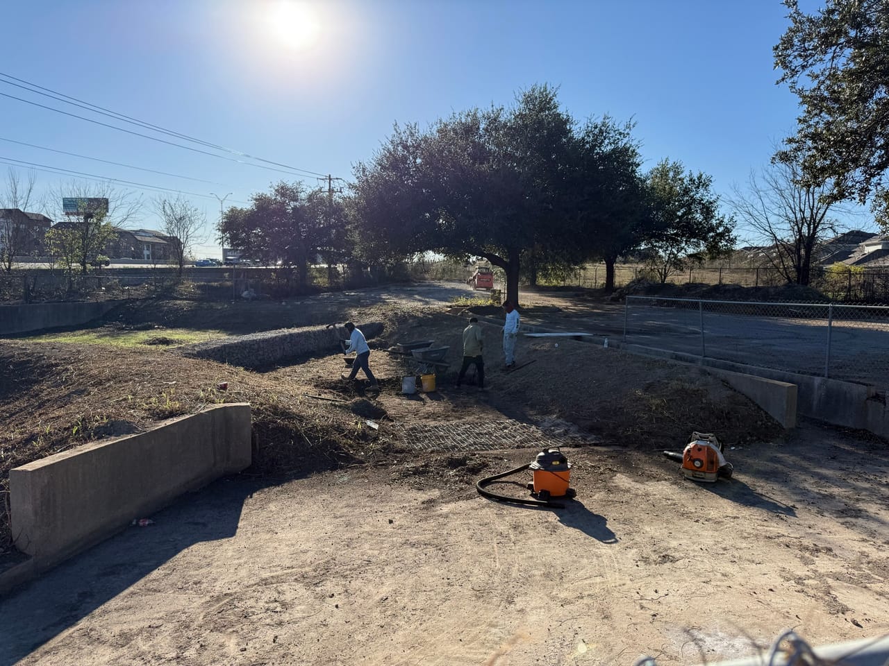 Crew cleaning a concrete basin with blowers under heavy sun glare in Central Texas