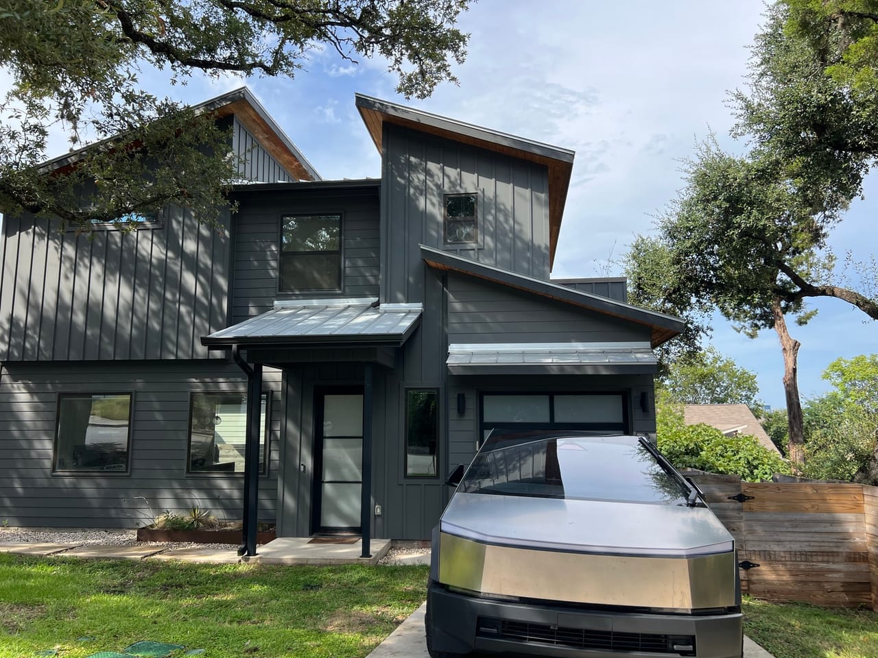 Modern gray home with parked car, oak tree and trimmed lawn in Maxwell, TX