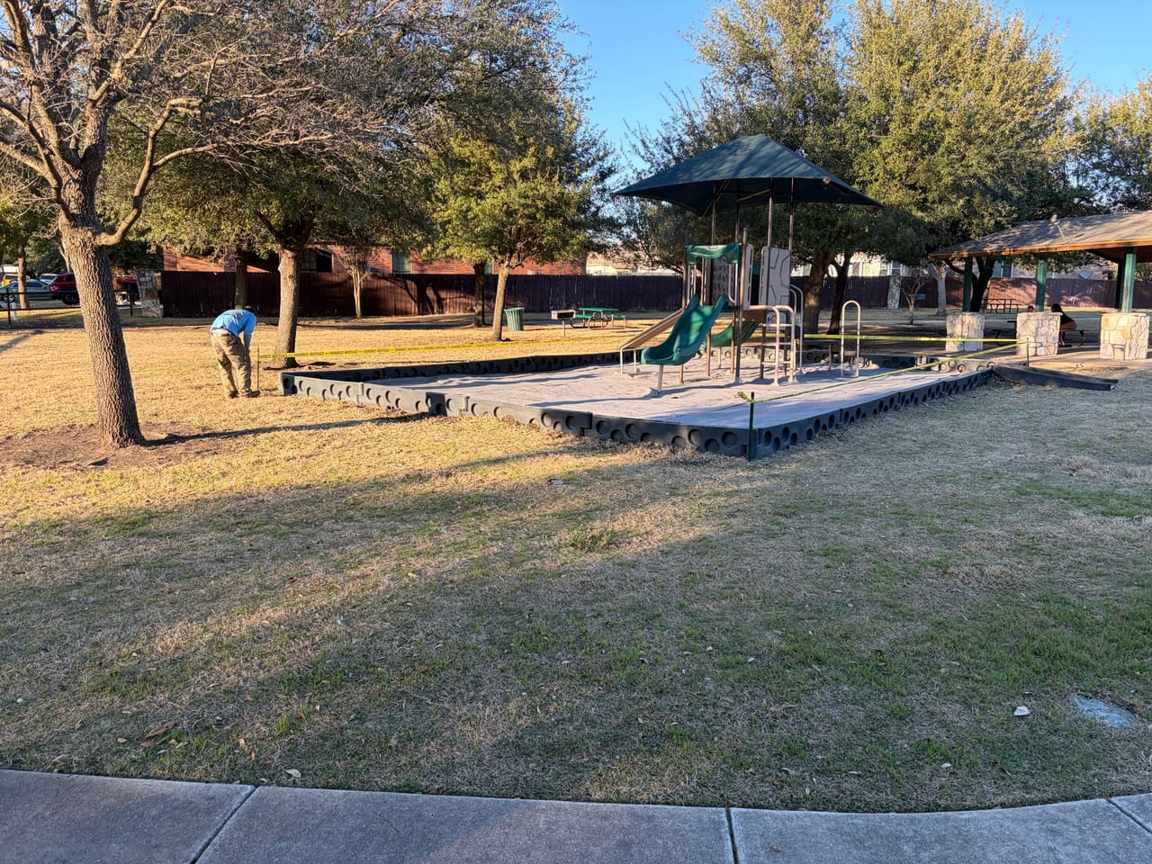 Neighborhood park playground and lawn with a worker in the distance in Central Texas