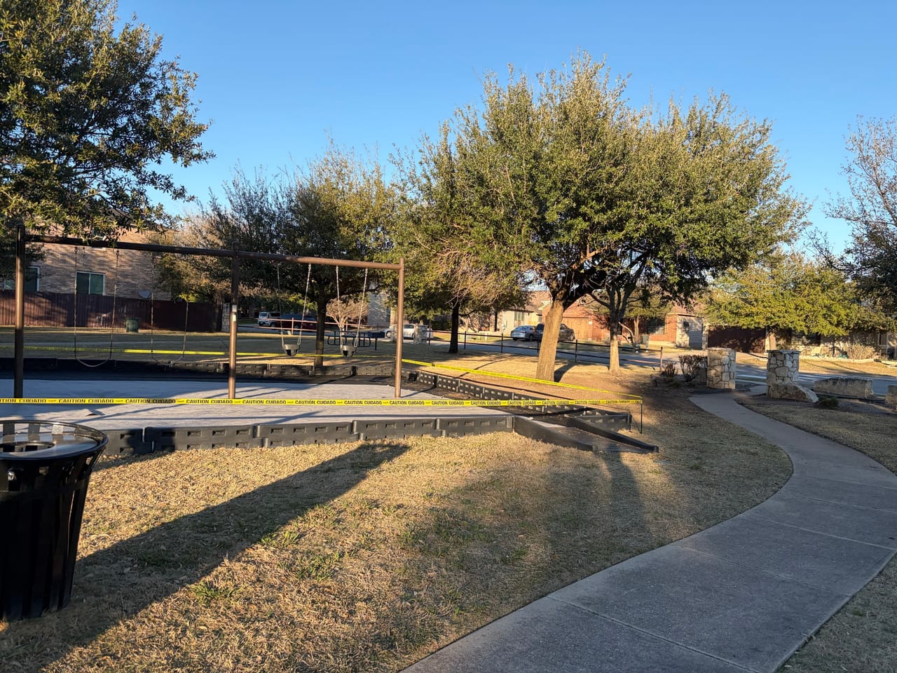 Park lawn and sidewalk with playground equipment behind the trees in Central Texas