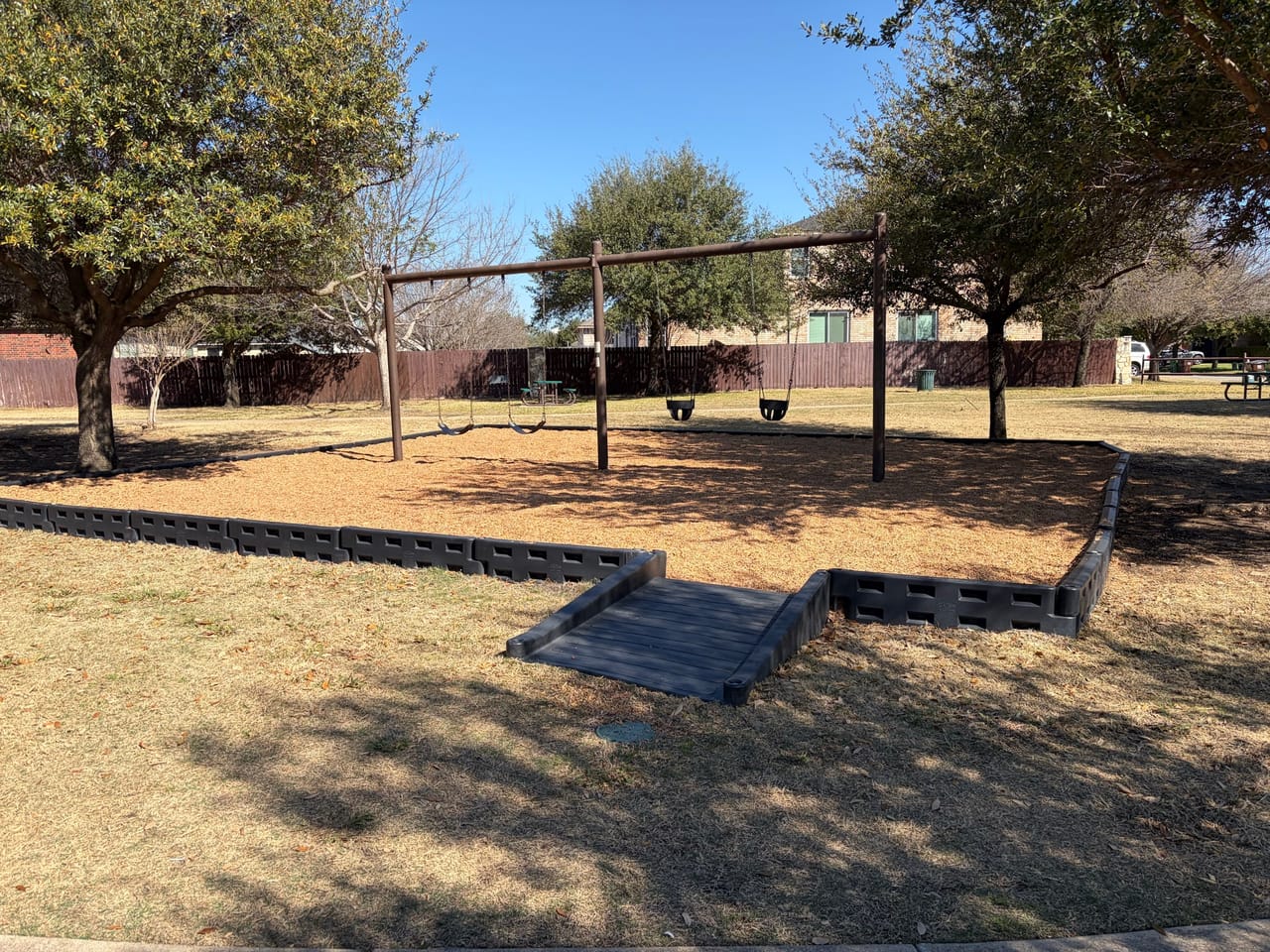 Park swing set and bordered bed on winter dormant turf in Central Texas