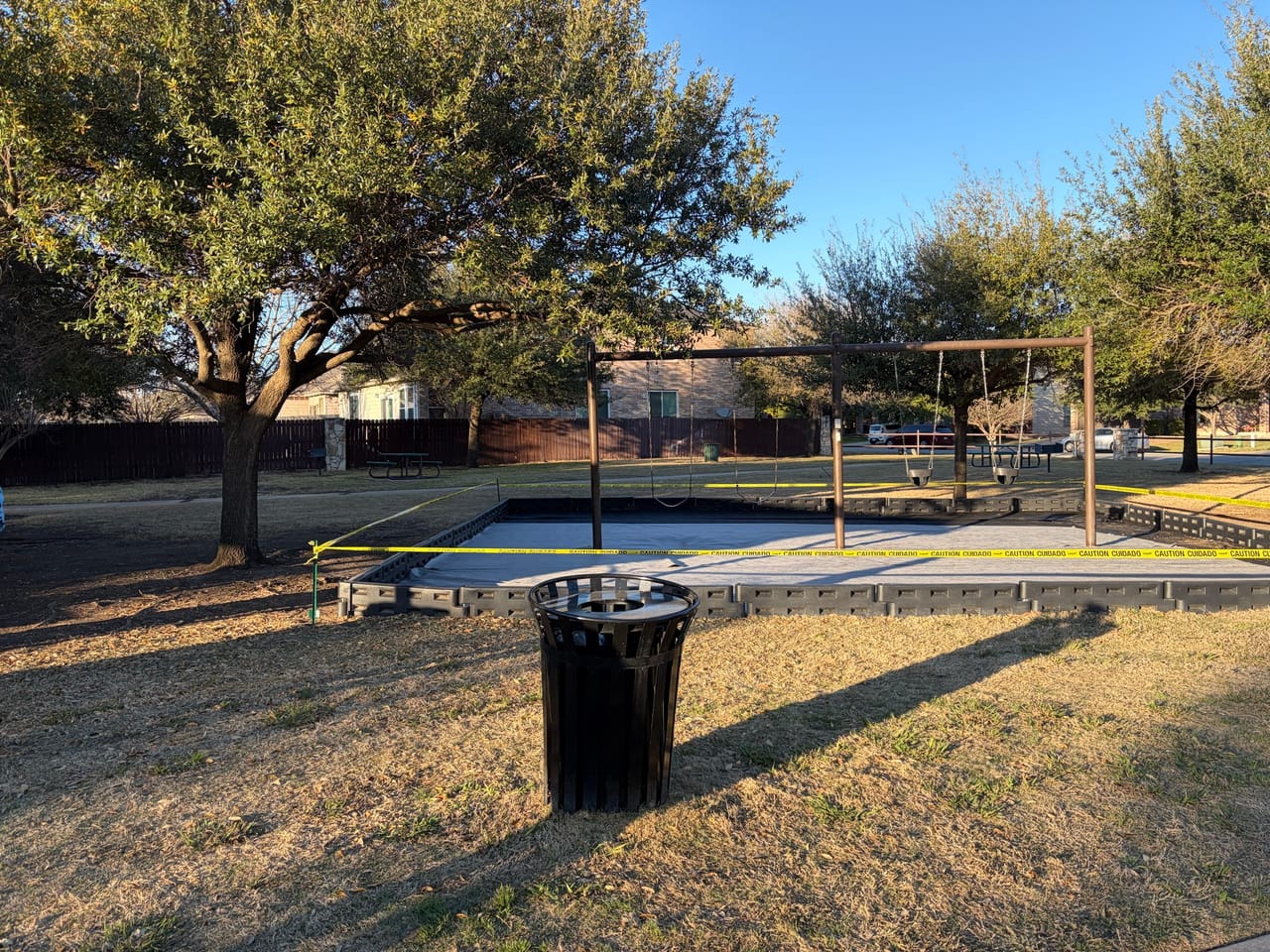 Park swing sets and trash can on dormant winter grass in Central Texas
