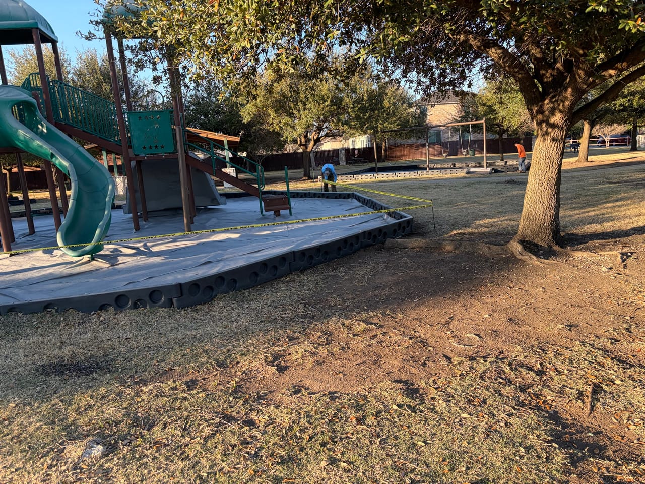 Playground and shade trees with cleared bed around the equipment in Central Texas
