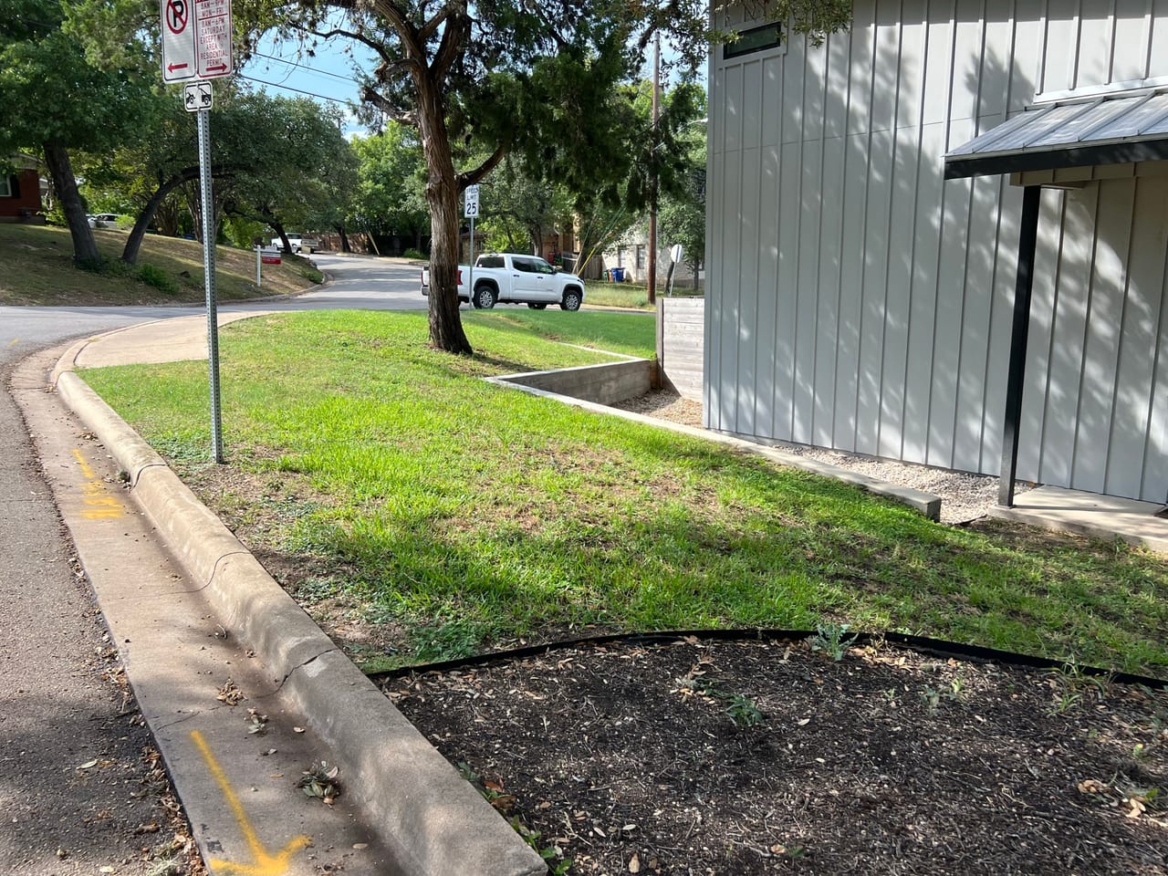 Sidewalk and lawn strip beside a building with mulch bed in Central Texas
