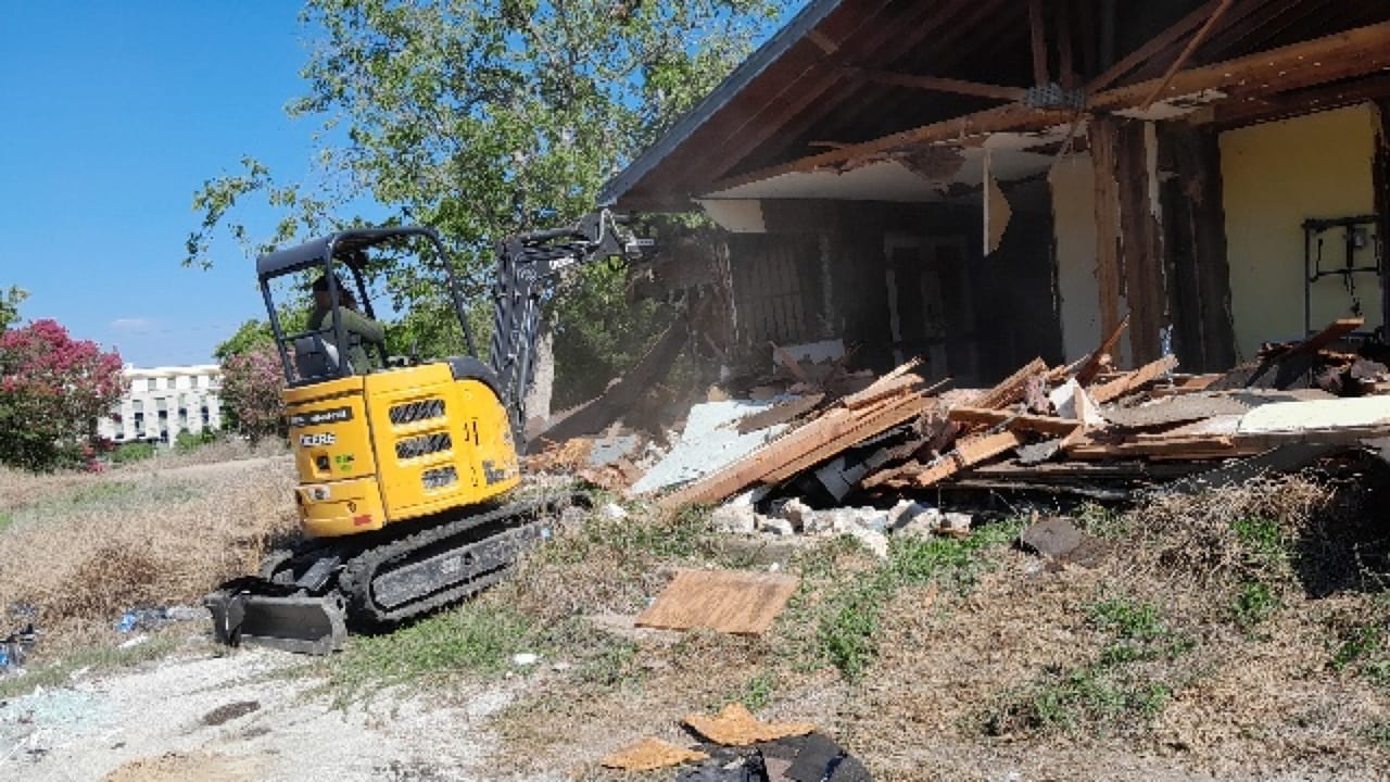 Excavator pulling down a house wall with lumber debris piled up in Bastrop, TX