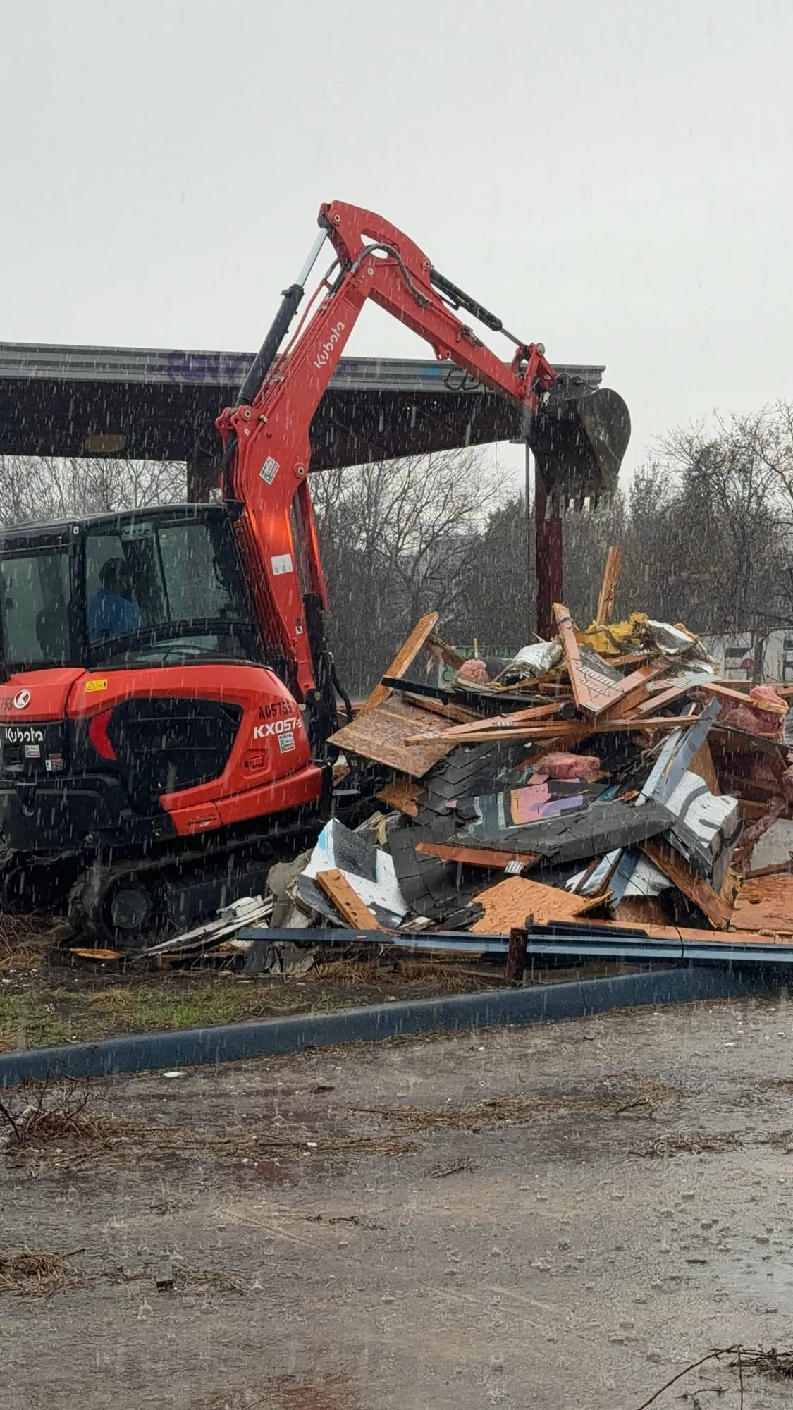 Kubota excavator beside a tall pile of demolished building debris in rain in Round Rock, TX