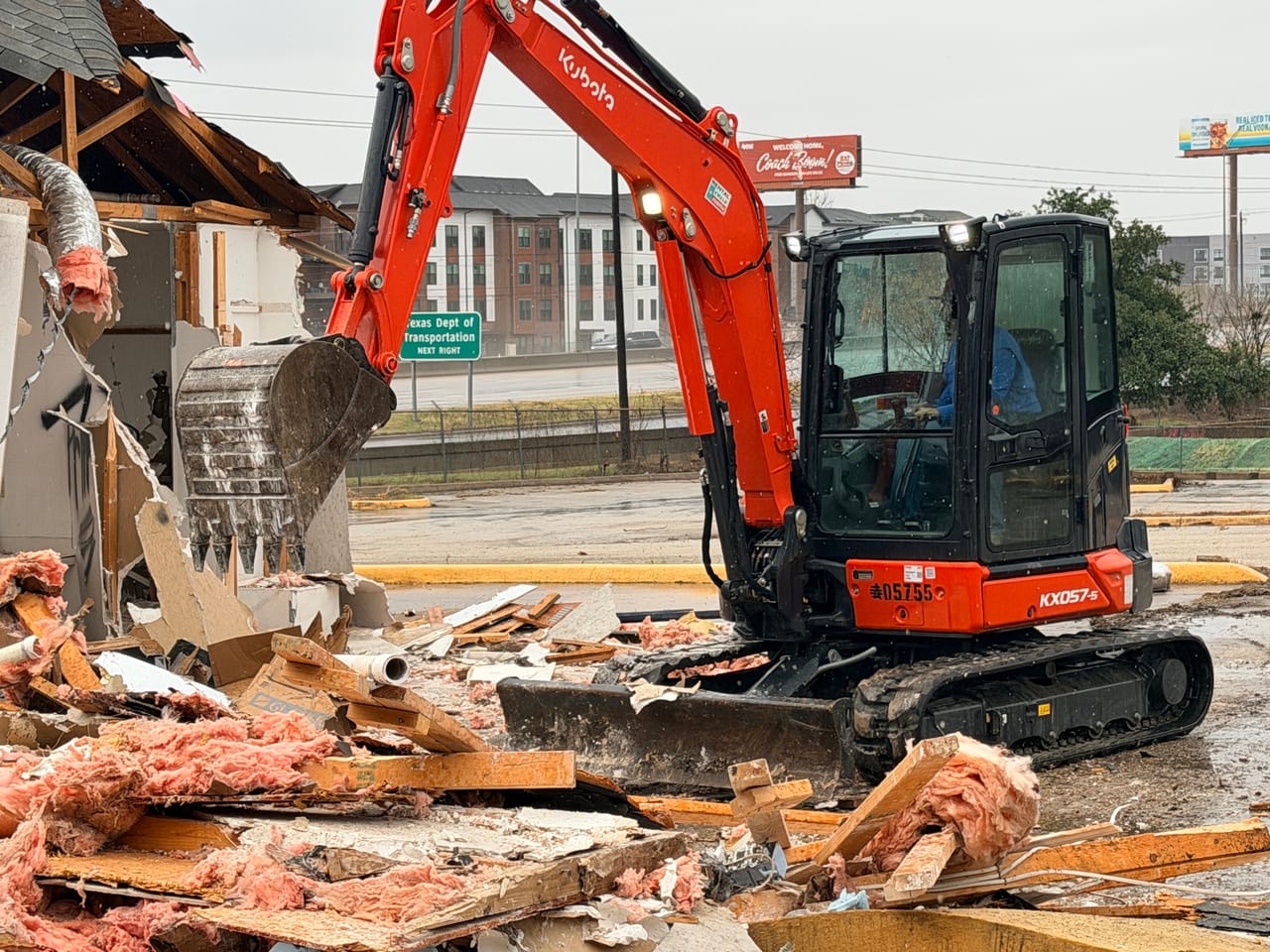 Kubota excavator tearing down a wood structure beside a lumber debris pile in Pflugerville, TX