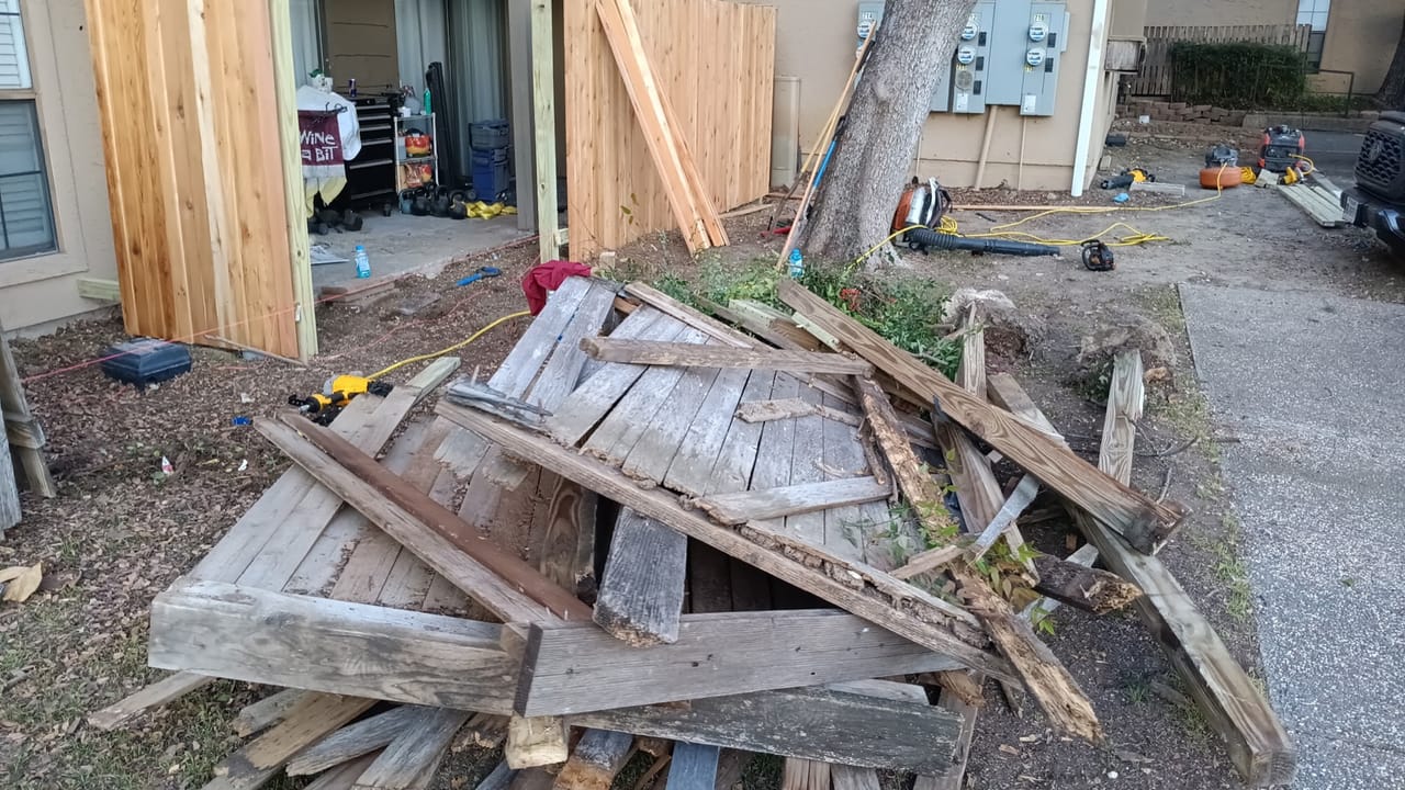 Pile of old wood fence pickets torn out and stacked beside a tree in Central Texas