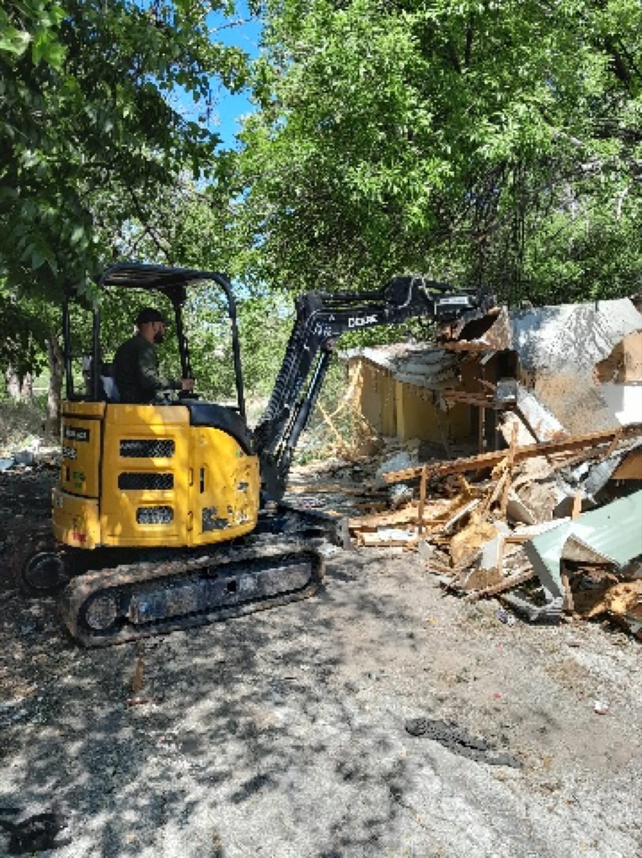Yellow excavator tearing down a small structure into a debris pile in Buda, TX