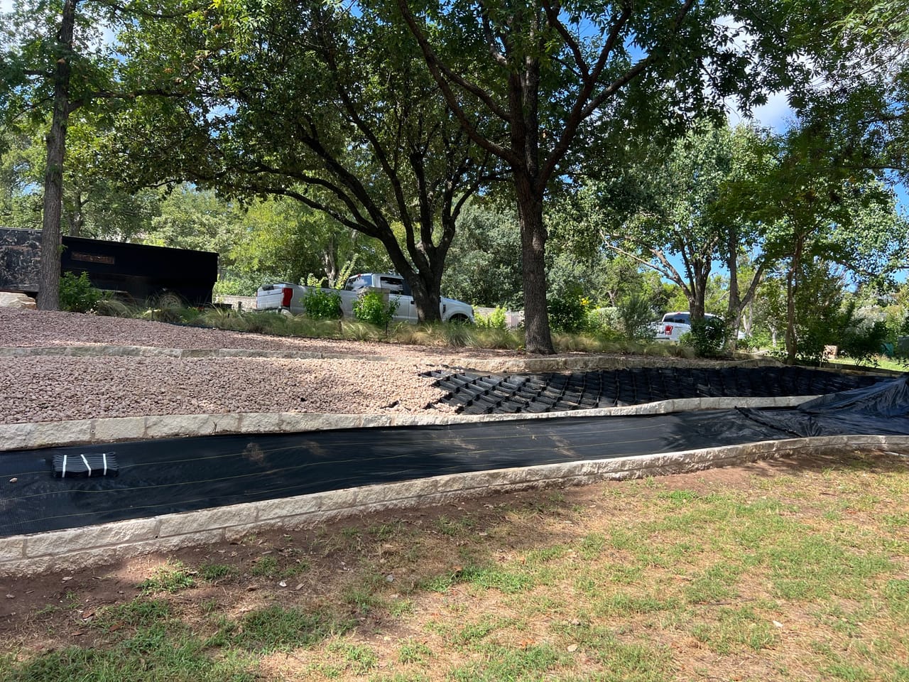Black geocell matting section of drainage channel under large oak trees in Taylor, TX