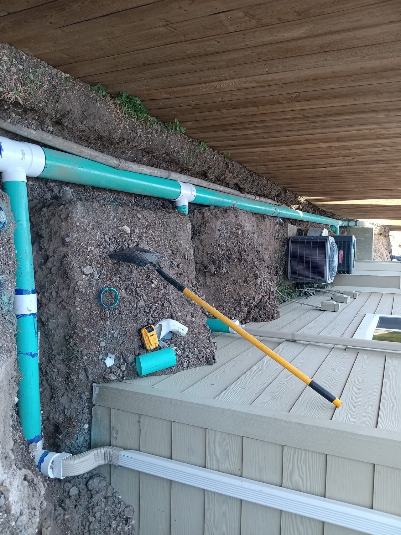 Blue PVC drain lines set in a trench along a foundation under decking in Round Rock, TX