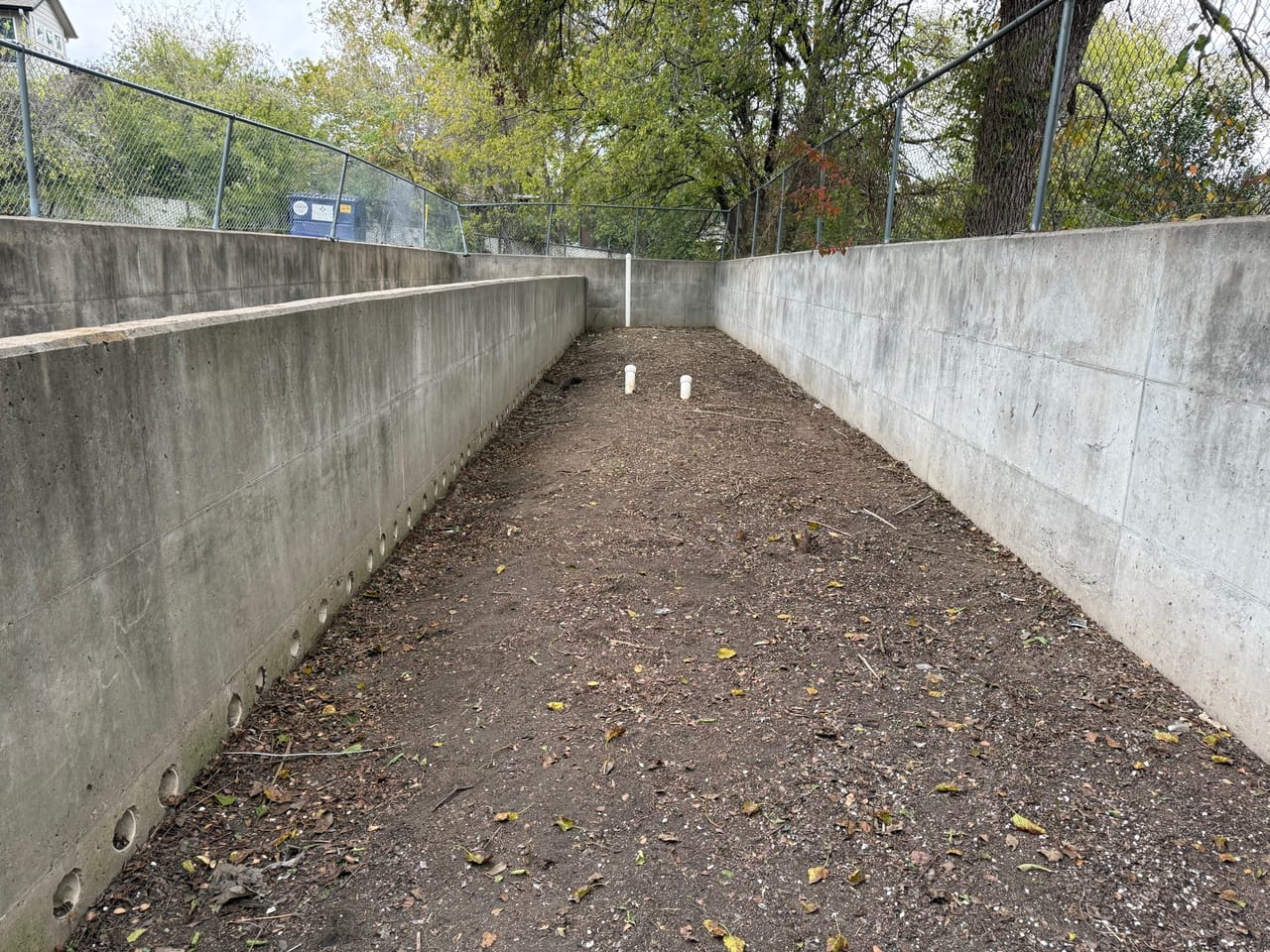 Cleaned concrete drainage channel with smooth walls and swept dirt bottom in Kyle, TX