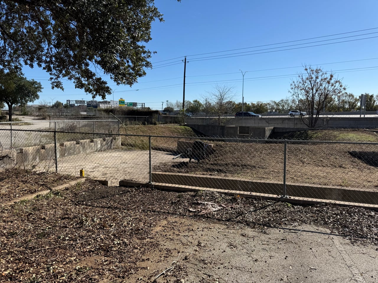 Cleared dirt drainage swale running along the edge of a parking lot in Leander, TX