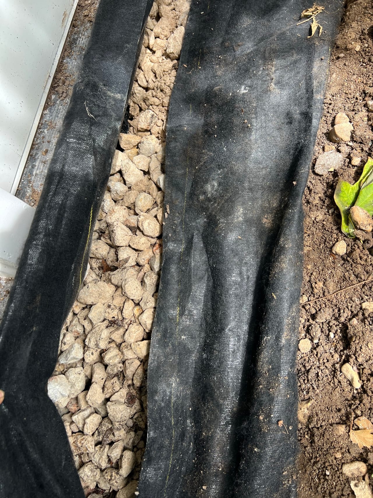 Close up of a french drain trench lined with fabric and gravel in Austin, TX