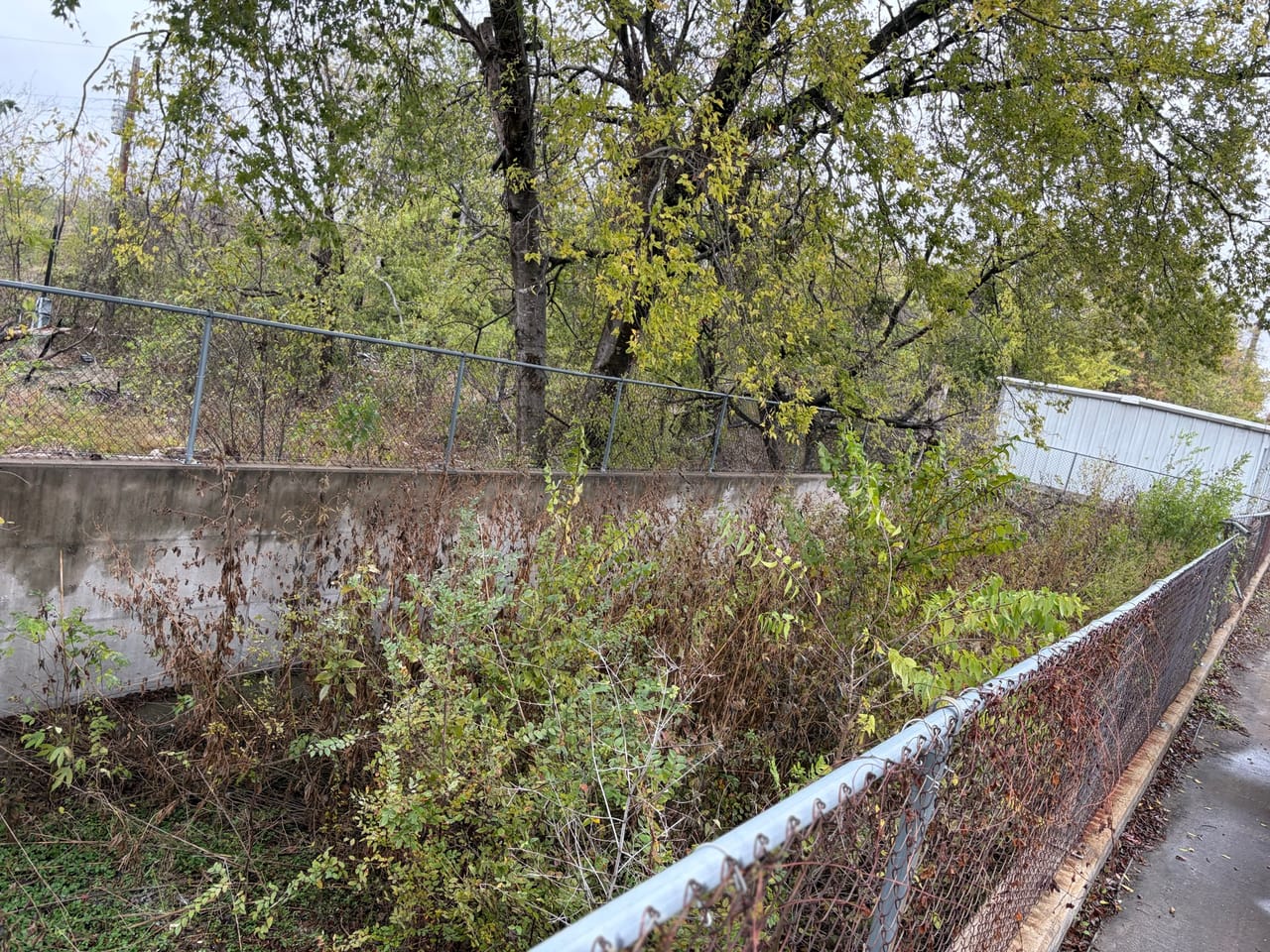 Concrete channel with brush along the bank and rusty fence line in Buda, TX
