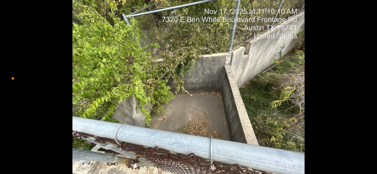 Concrete channel headwall buried in heavy vegetation beside a guardrail in Lakeway, TX