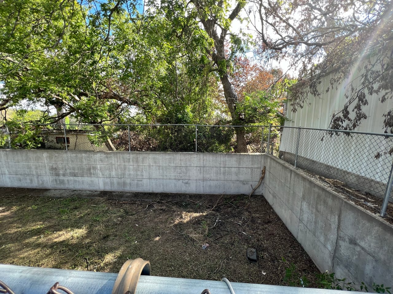 Concrete retaining wall along a cleared yard with drain pipe in Central Texas