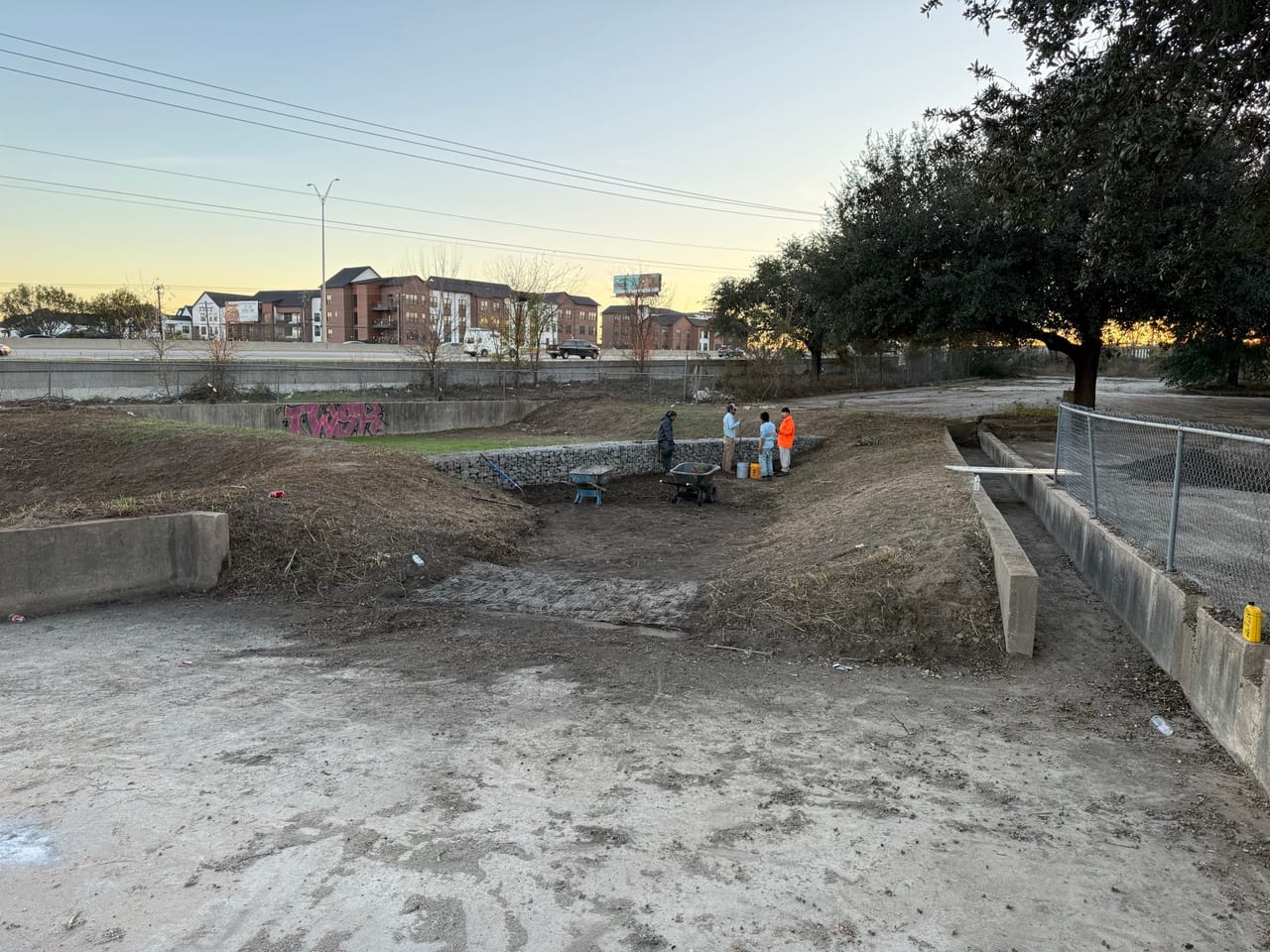 Crew clearing a concrete drainage channel and dirt basin at dusk in Georgetown, TX