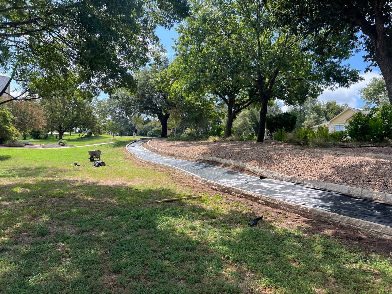 Curving gravel swale edging a shaded lawn beside a residential street in Central Texas