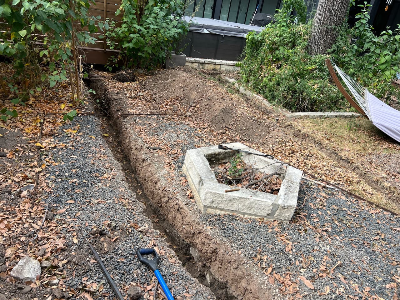 Curving trench across a yard past a limestone fire pit ring in Leander, TX