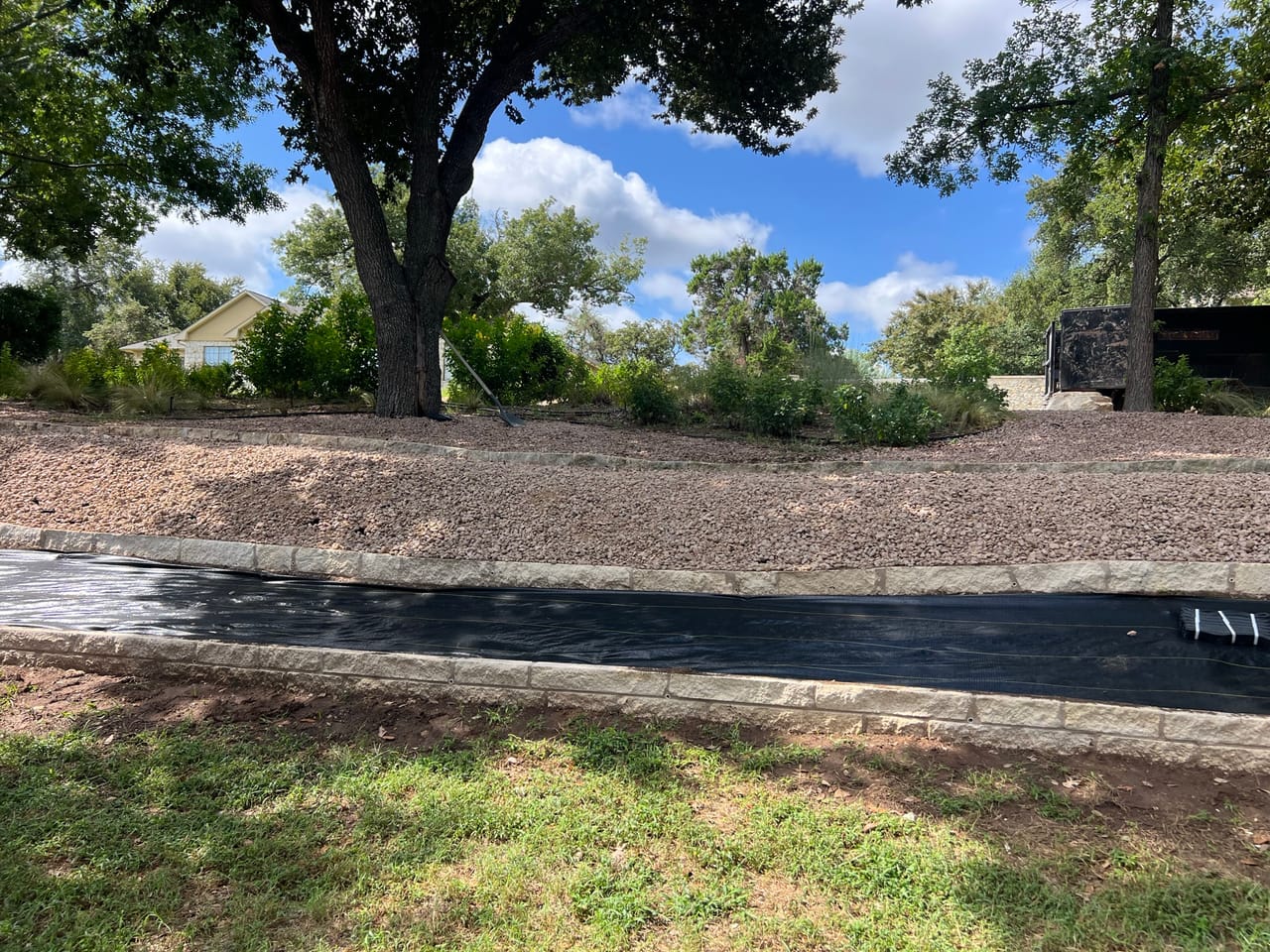 Finished rock drainage channel through shaded lawn near a stone wall in Central Texas