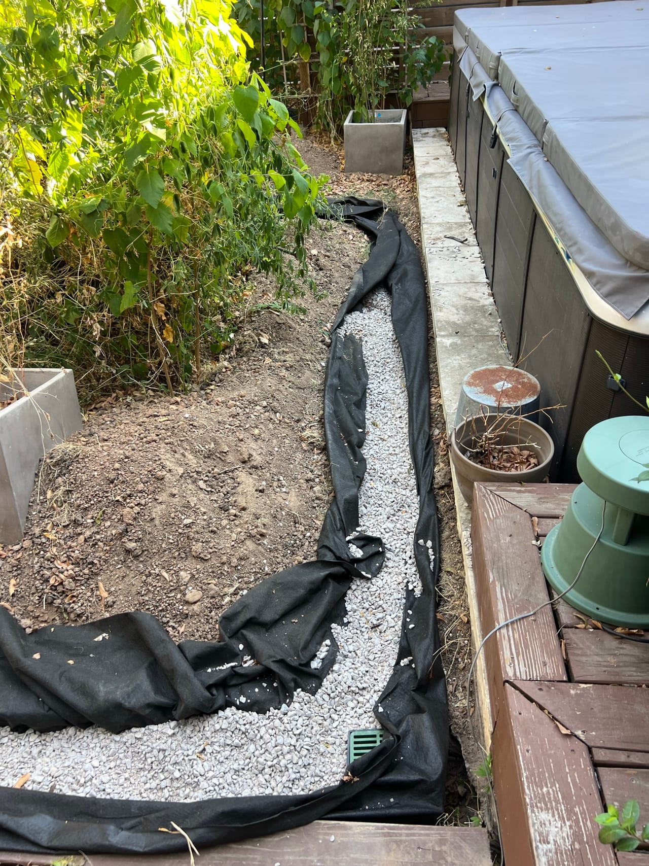 French drain trench lined with black fabric and gravel by deck in Lakeway, TX
