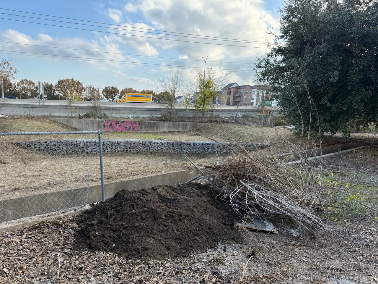 Large pile of excavated silt and brush beside a concrete channel in Central Texas