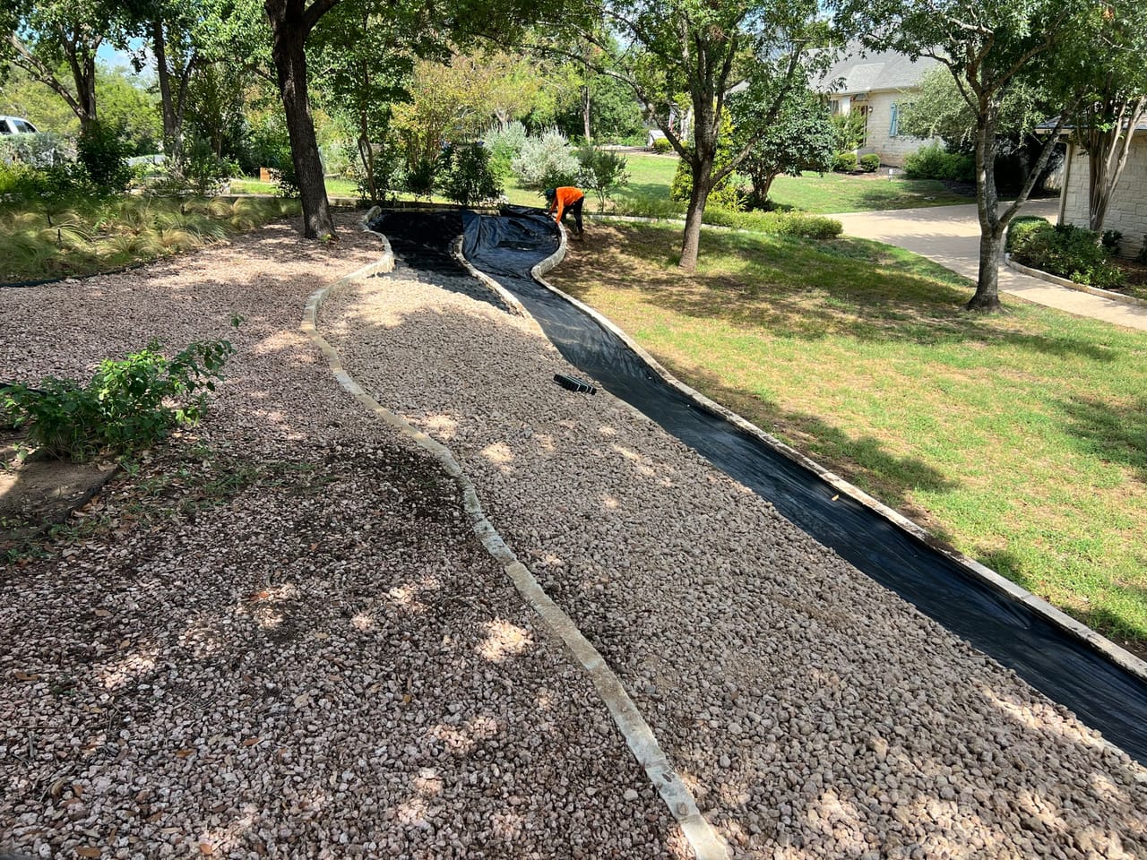 Long dry creek channel with black matting winding across a lawn in Leander, TX