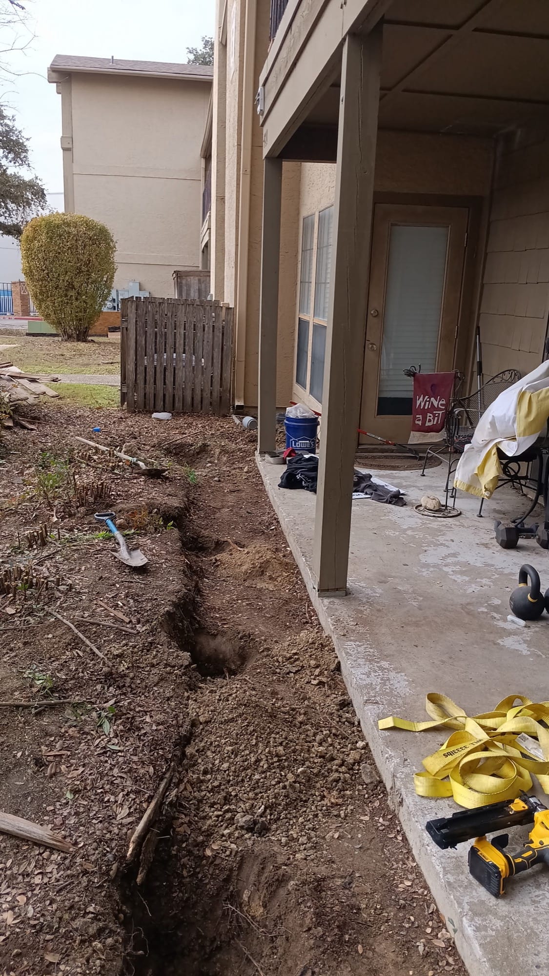 Narrow trench dug along a building foundation with a shovel resting nearby in Buda, TX