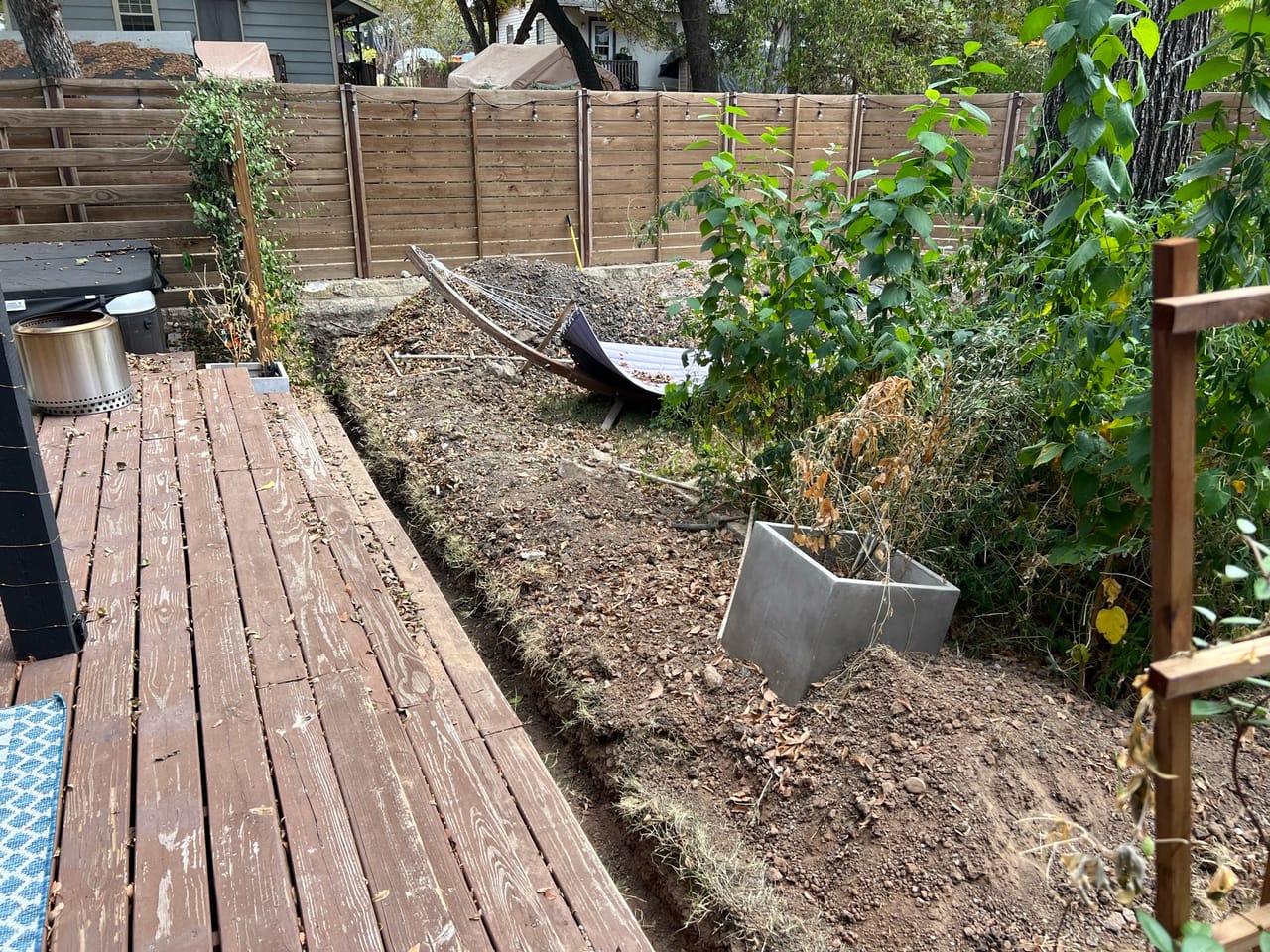 Open trench dug alongside a wood deck in a fenced backyard in Kyle, TX