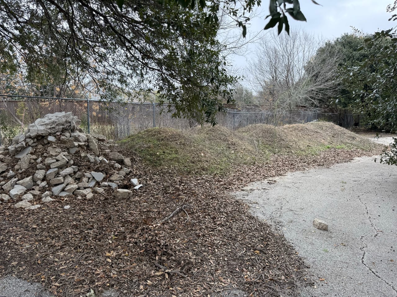 Rock pile beside a cleared dirt drainage swale near a fence in Bee Cave, TX