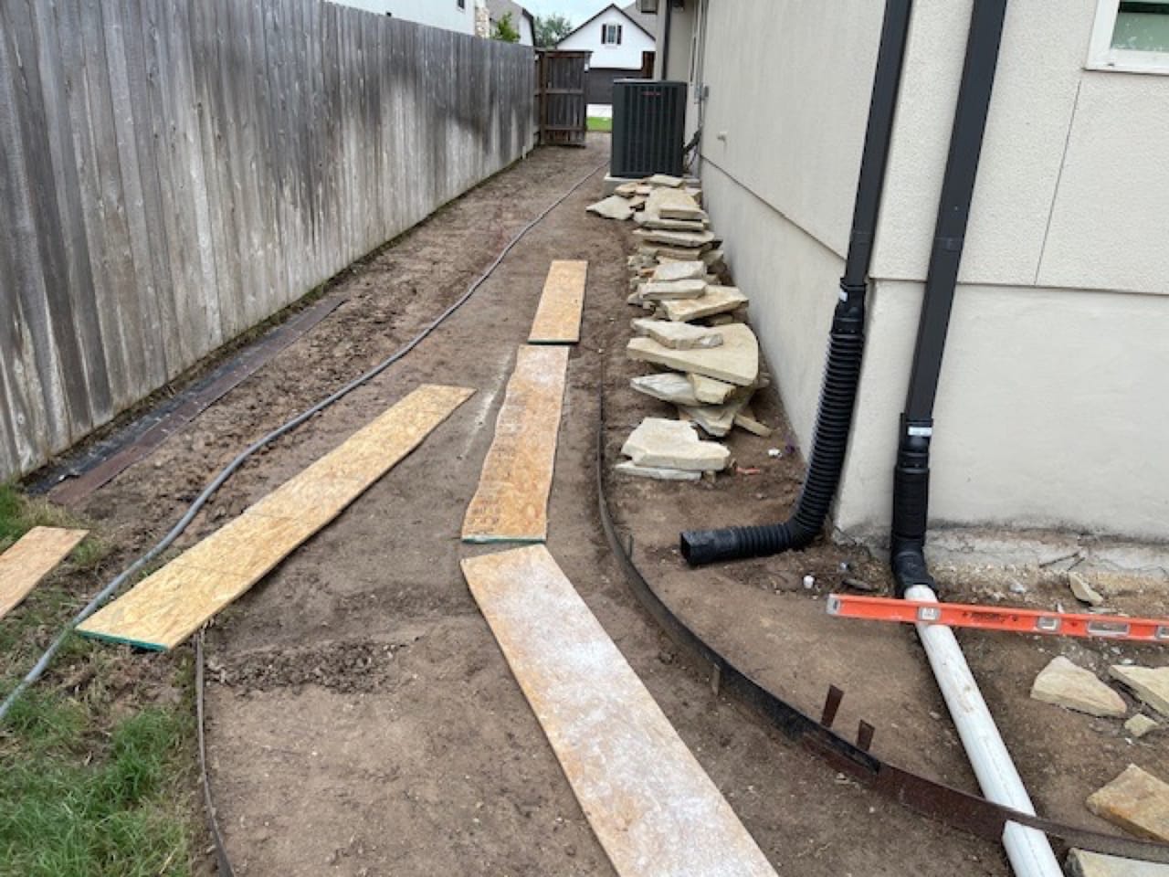 Side yard trench with corrugated downspout drain lines and staged flagstone in Austin, TX