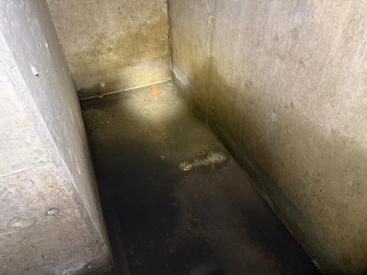 Sunlit corner of a concrete stormwater vault with water on the floor in Central Texas