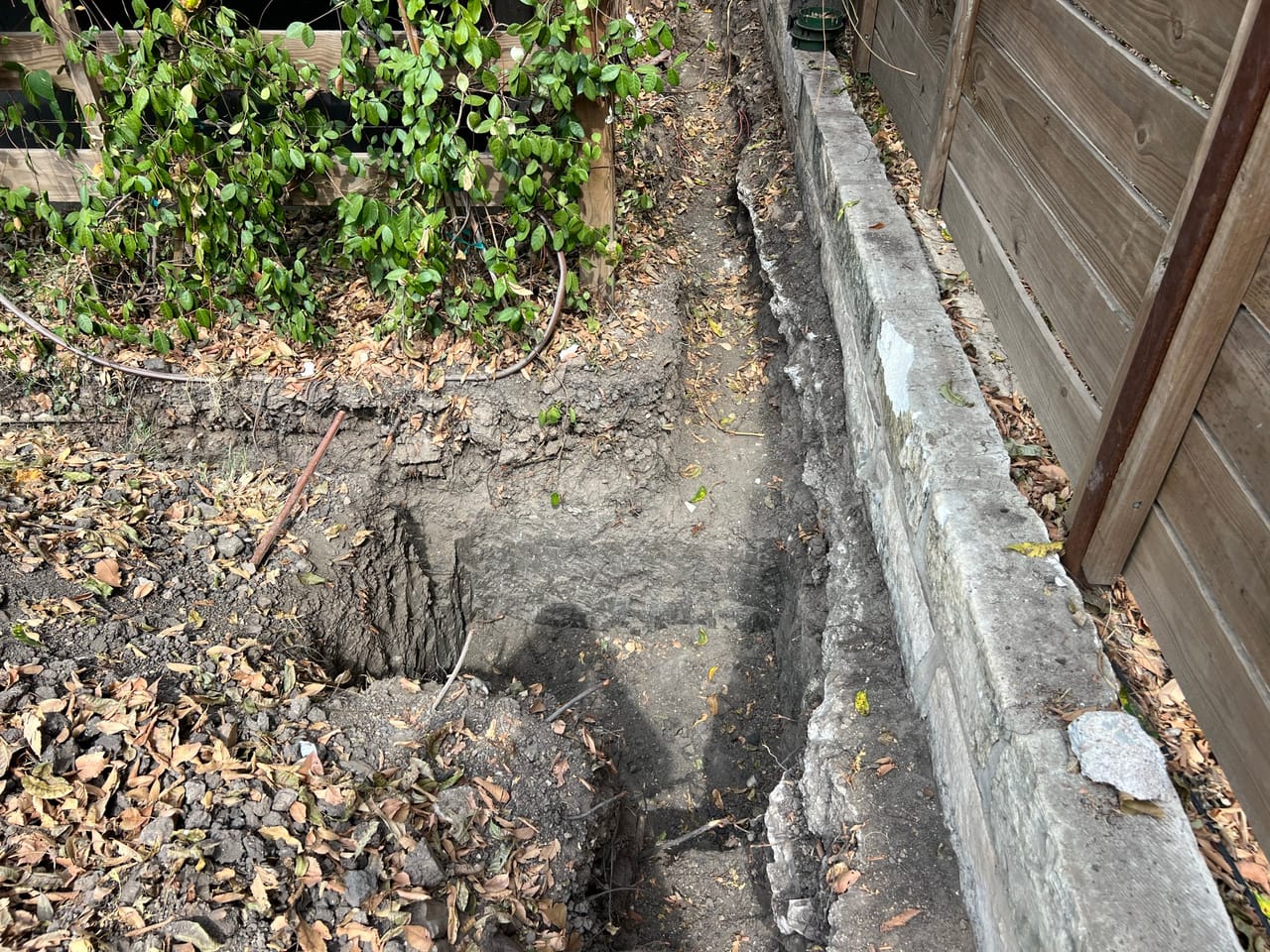 Trench along fence with gravel, exposed soil and plant bed in Central Texas