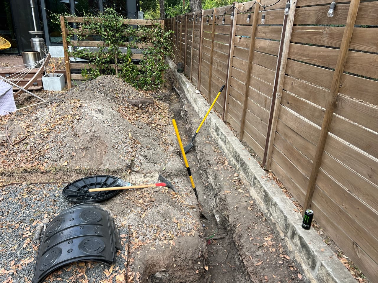 Trench along a wood fence with drain basin and soil piles in Elgin, TX