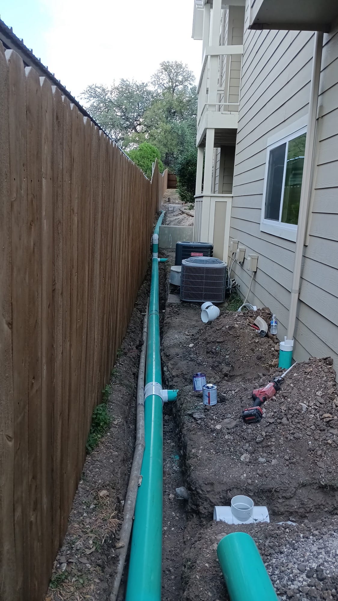Trench with green drain pipe running along a house past condenser units in Pflugerville, TX