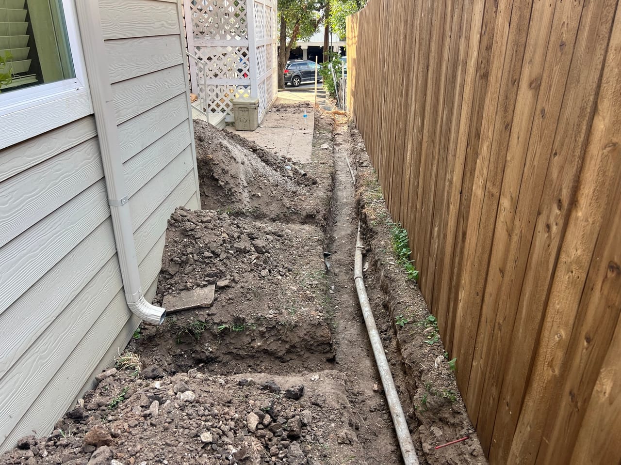 Trench beside a house with downspout drain pipe and wood fence in Bastrop, TX