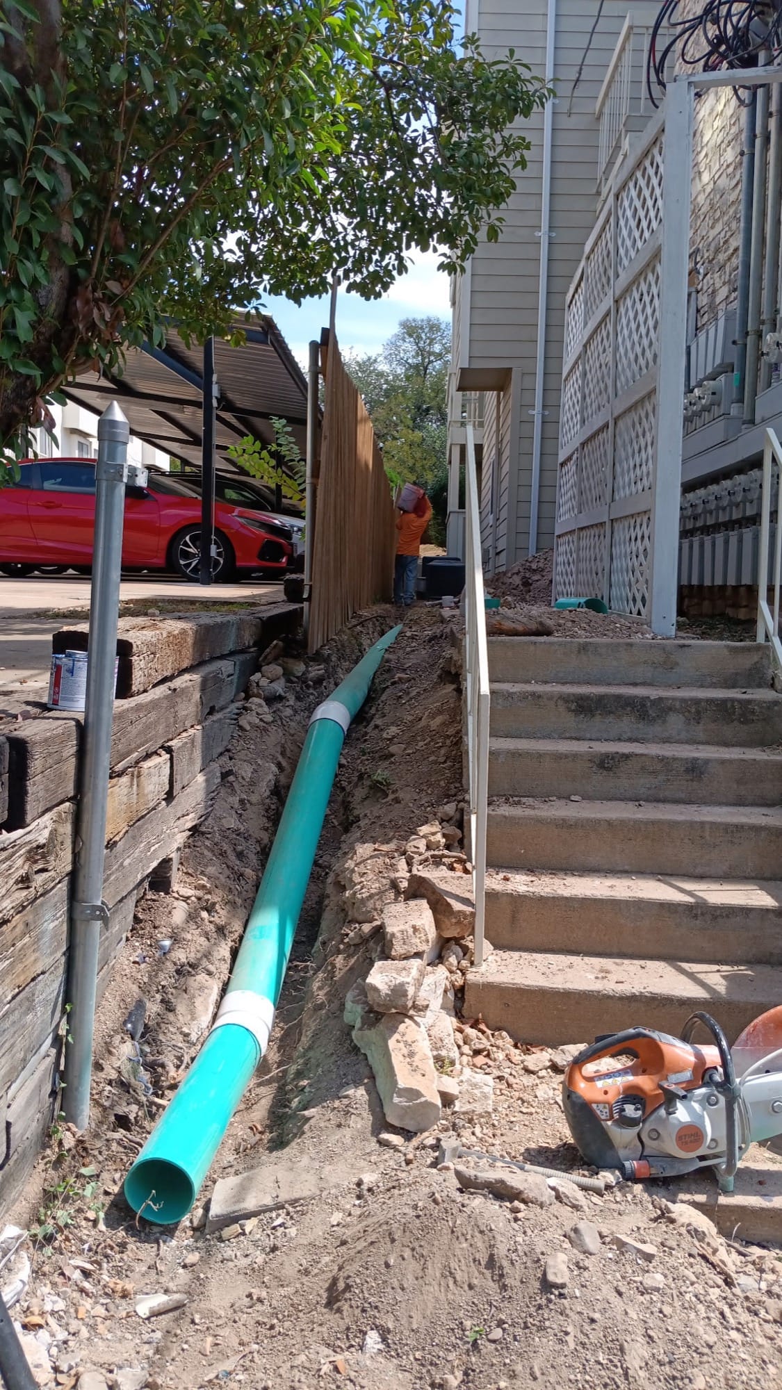 Trench with large green drain pipe beside a timber wall and steps in Leander, TX