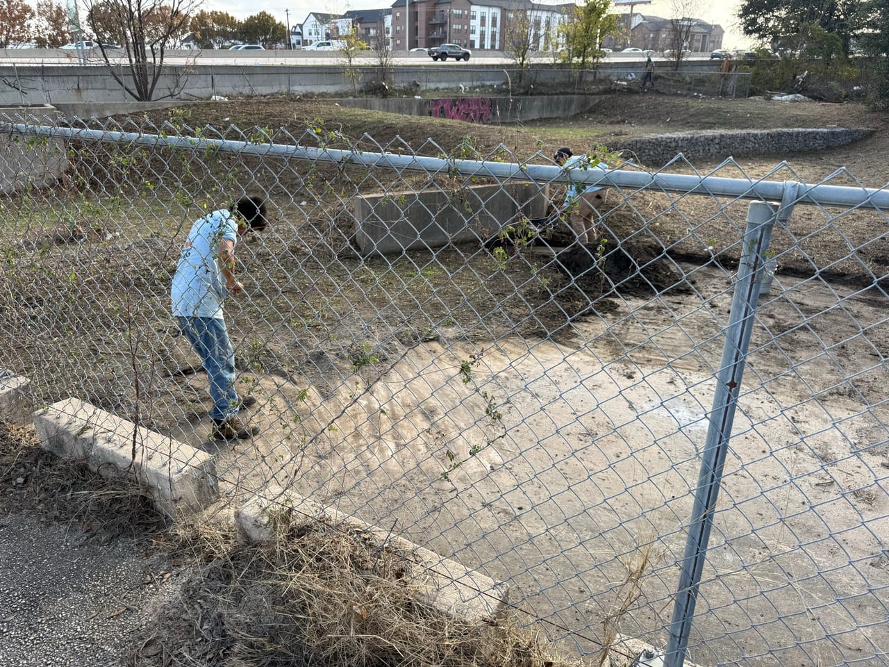 Worker at chain link fence above a cleared concrete drainage channel in Kyle, TX
