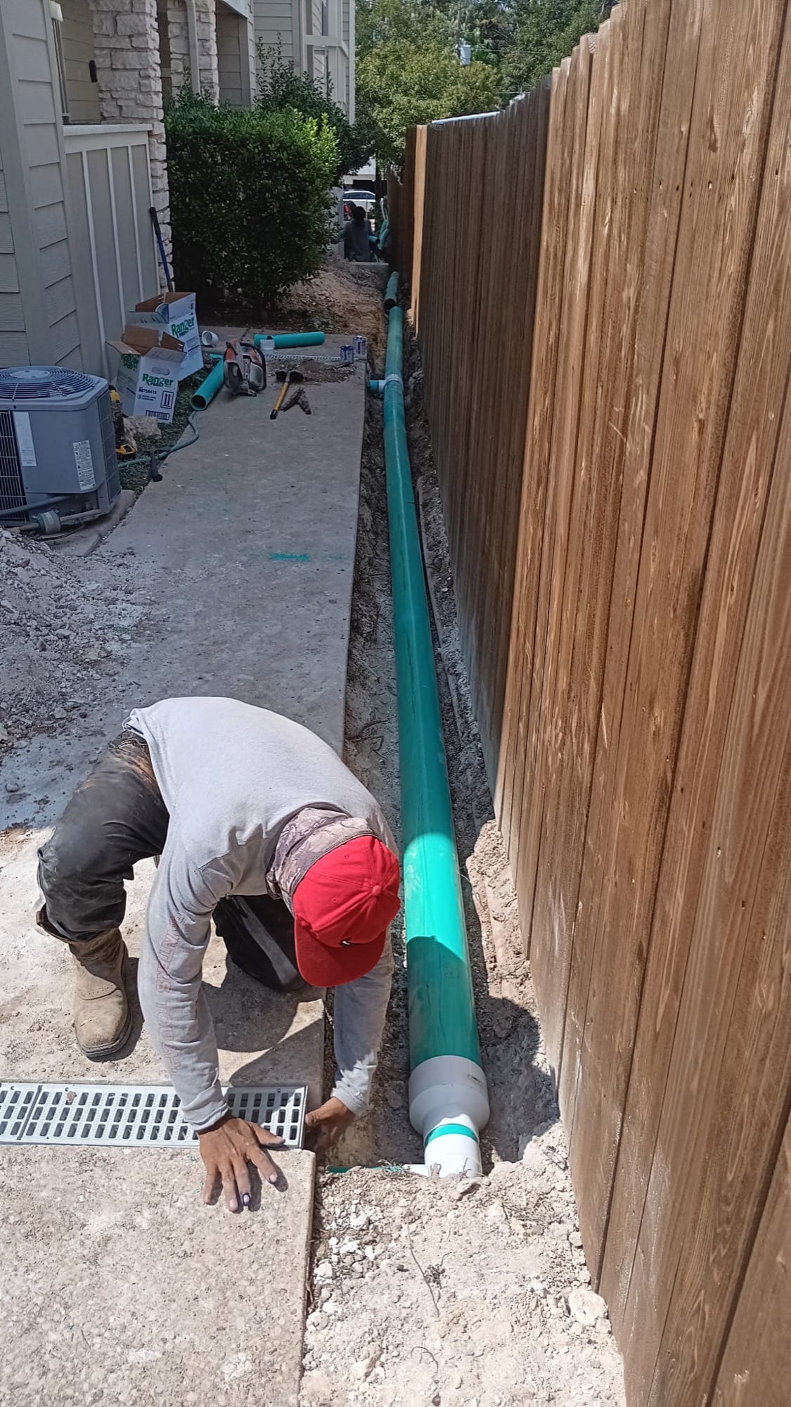 Worker crouched installing a green drain pipe against a wood fence in Taylor, TX