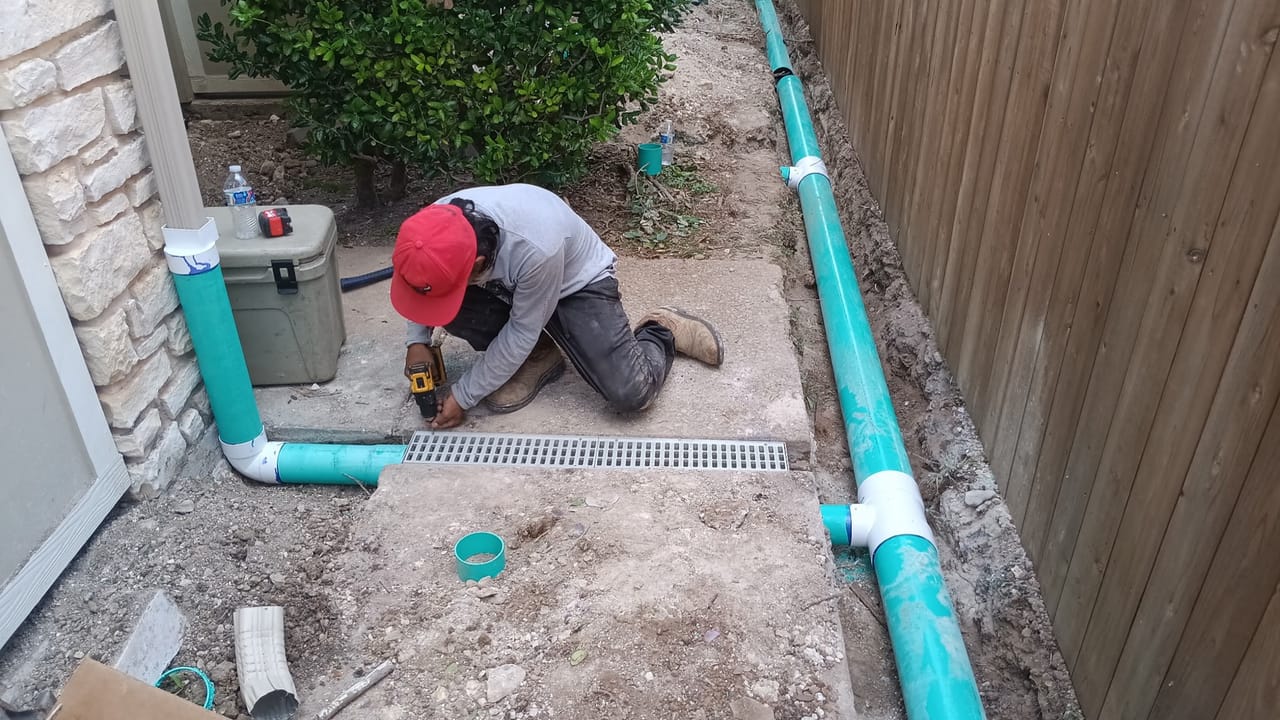 Worker installing a channel drain grate with blue PVC along a wall in Bastrop, TX