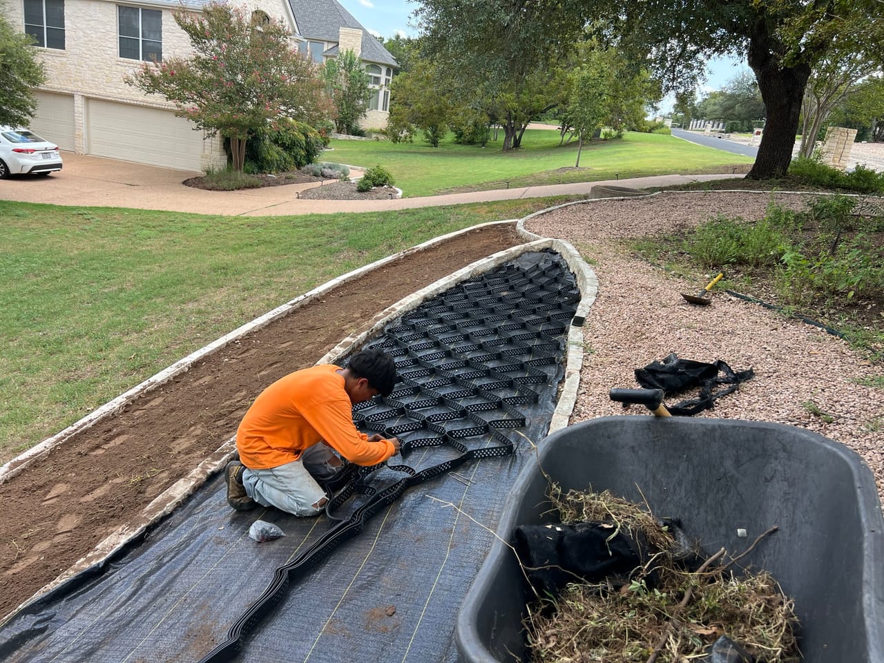Worker in orange laying black erosion matting in a drainage swale in Pflugerville, TX