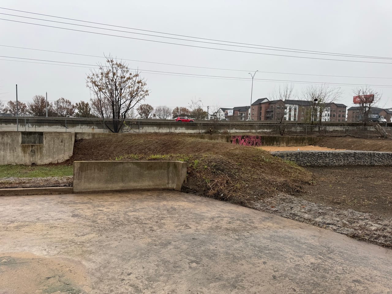 Concrete channel wall beside freshly graded dirt and a low headwall in Elgin, TX
