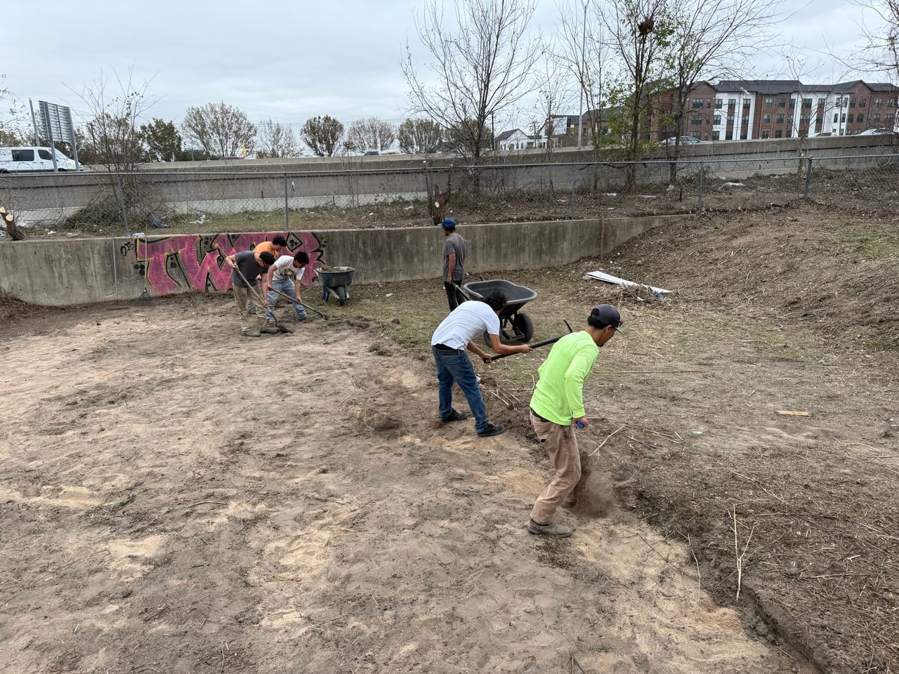 Crew grading a dirt detention basin beside a graffiti tagged wall in Bastrop, TX