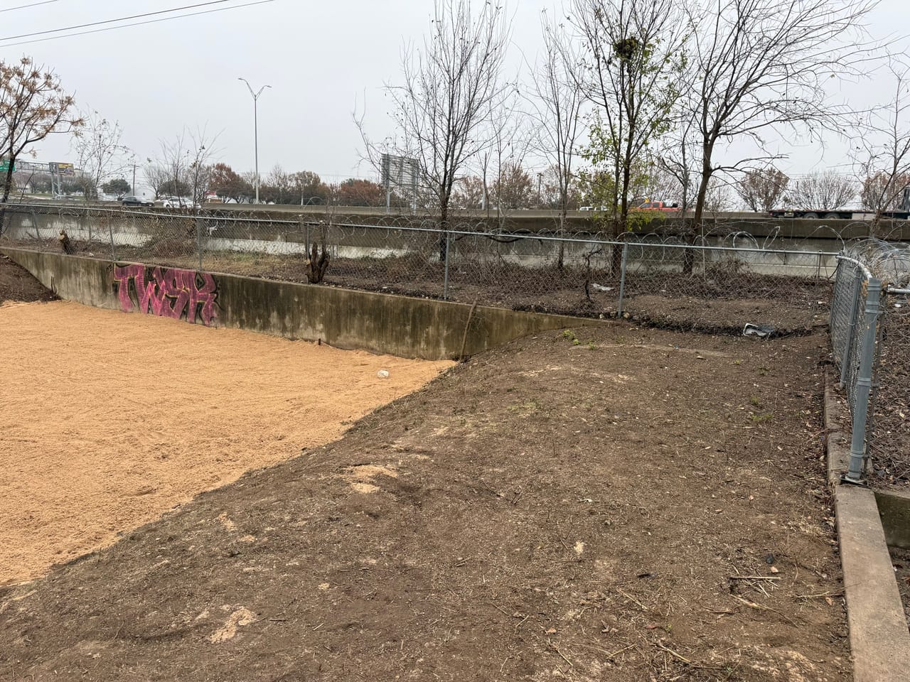 Freshly graded dirt basin floor inside the concrete drainage channel in Taylor, TX