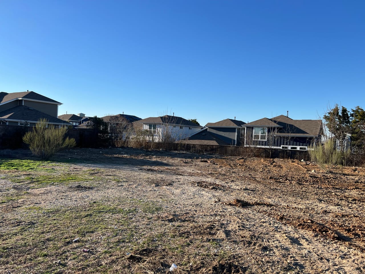 Freshly graded dirt lot with houses along the back fence in Leander, TX
