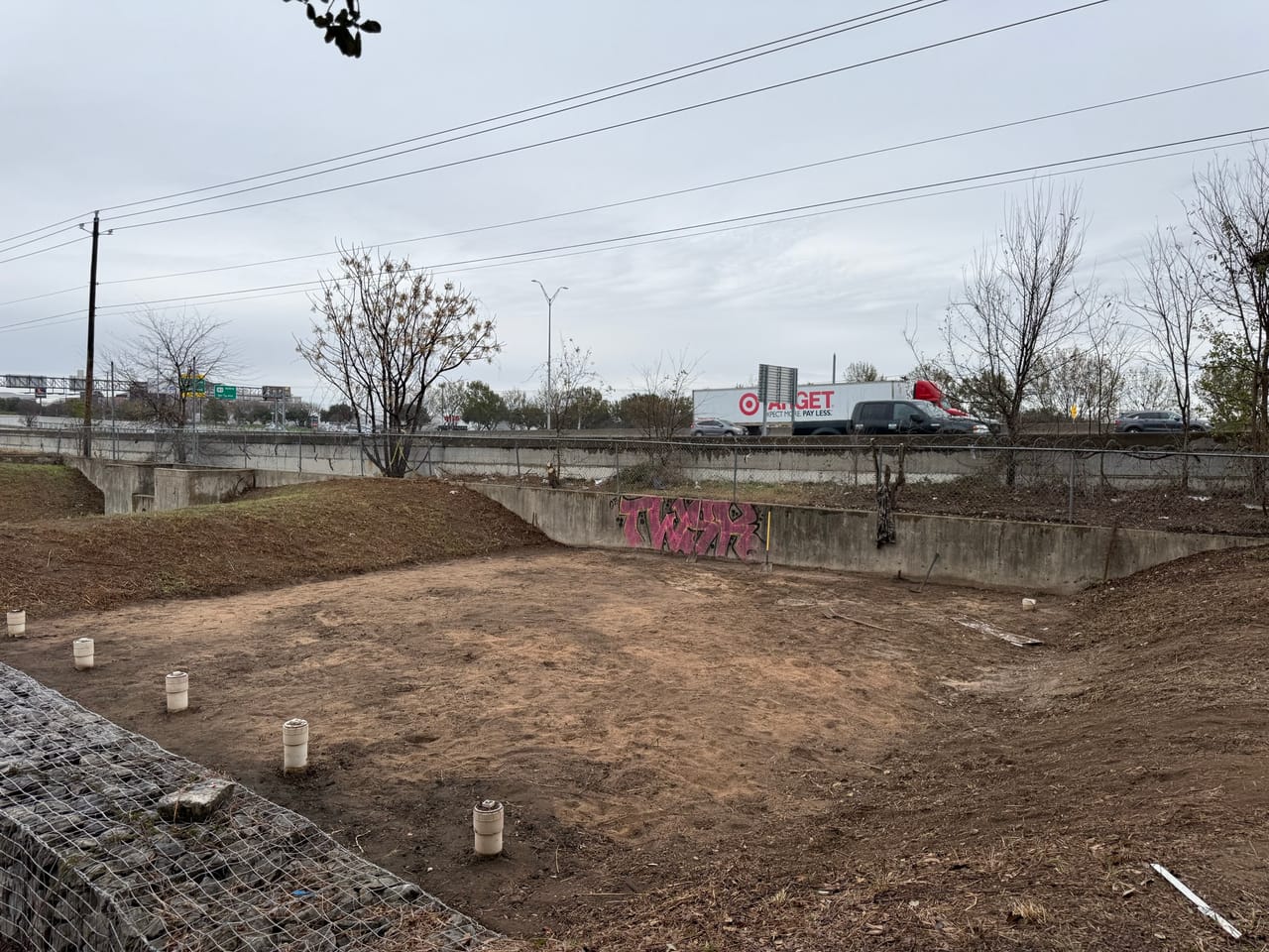 Graded dirt detention basin next to a highway and concrete wall in Pflugerville, TX