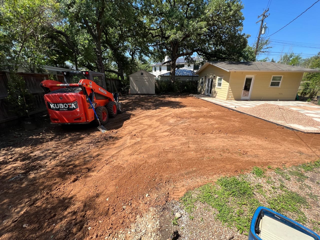 Orange Kubota skid steer on freshly graded dirt behind a house in Central Texas