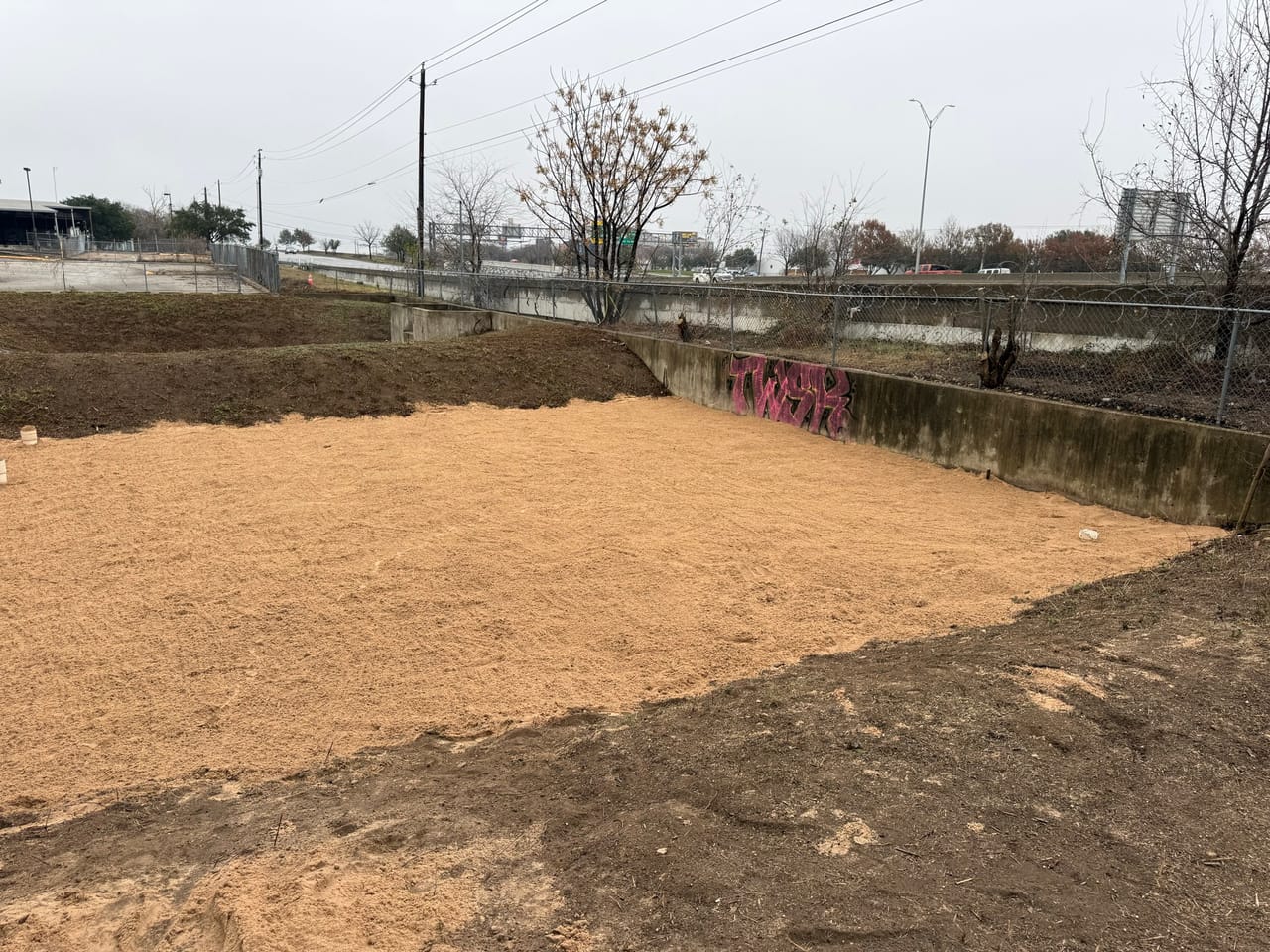 Smooth graded dirt basin with concrete retaining walls in the background in Buda, TX