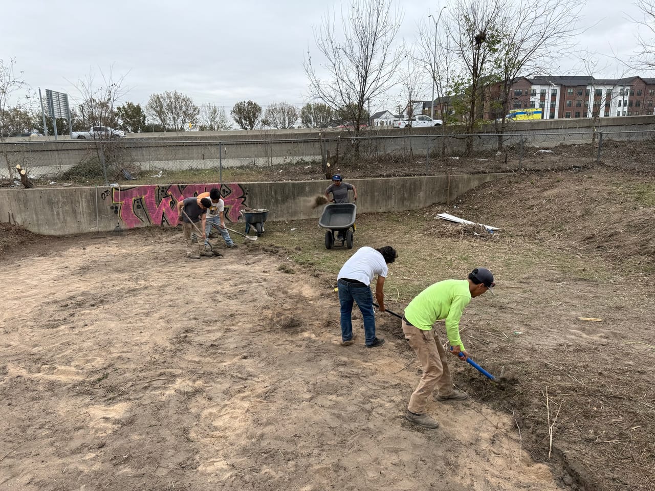 Two workers raking and shaping the bottom of a dirt basin in Round Rock, TX